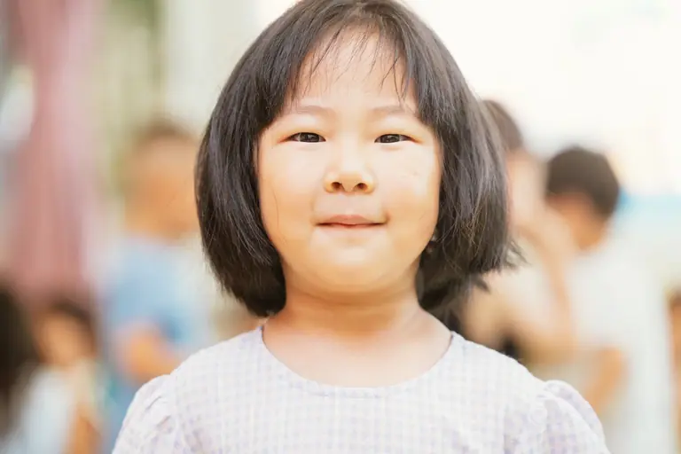 Charming portrait of an Asian girl smiling brightly in an outdoor setting with blurred background.
