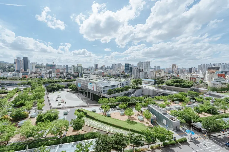 Aerial view of lush urban gardens and sprawling cityscape under a bright summer sky.