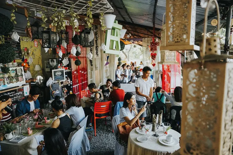 A lively indoor cafe with diverse patrons enjoying food and drinks amidst eclectic decor.