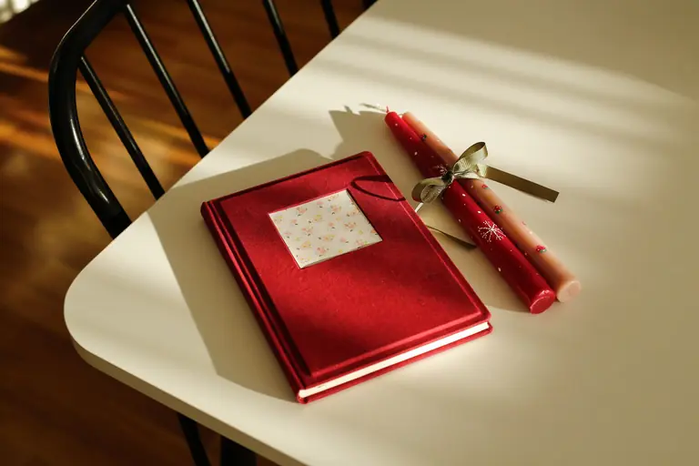 Elegant red journal and two decorative candles on a sunlit table, creating a warm ambiance.