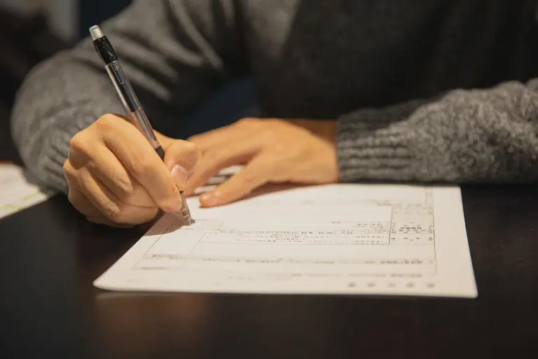 Crop anonymous male in gray sweater writing in form of important document at table