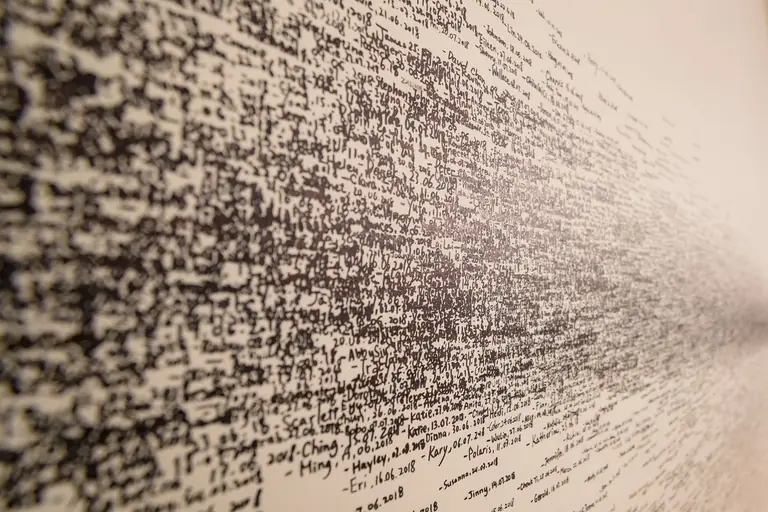Image of a wall covered with densely packed text creating an abstract pattern.