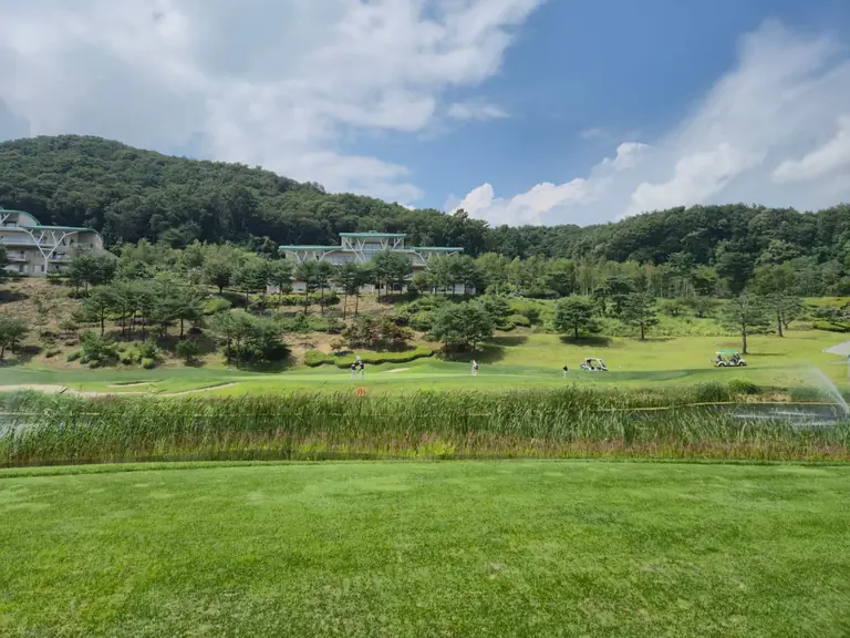A picturesque golf course set against lush greenery and a modern clubhouse, under a vibrant sky.