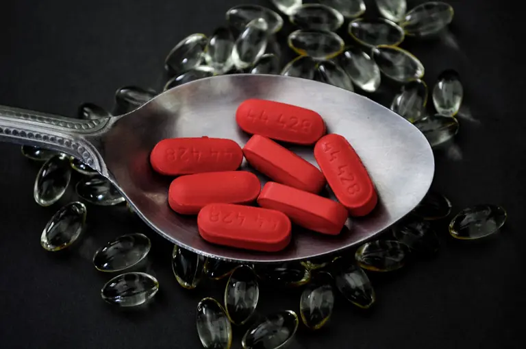 A detailed close-up of red pills on a spoon surrounded by transparent capsules.