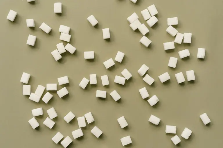 A top-down view of sugar cubes scattered over an olive green background.