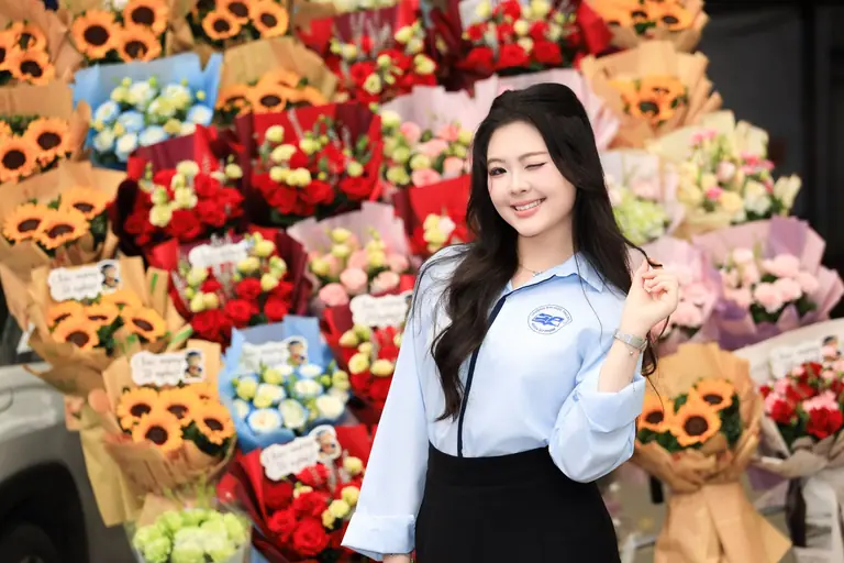 A cheerful woman winks while surrounded by a vibrant display of flower bouquets, symbolizing joy and celebration.