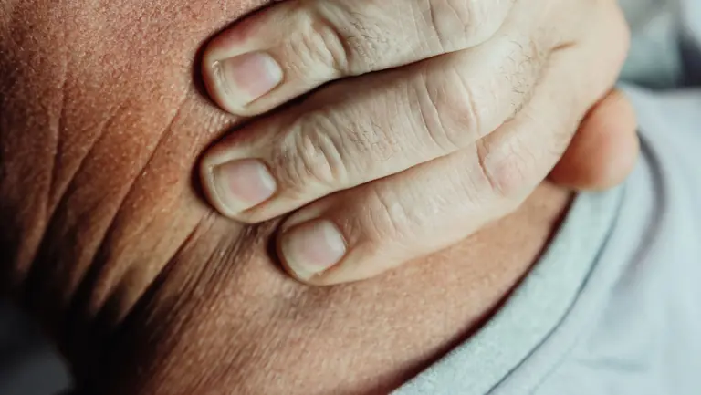 A detailed close-up of a person's hand touching their neck, suggesting pain or discomfort.
