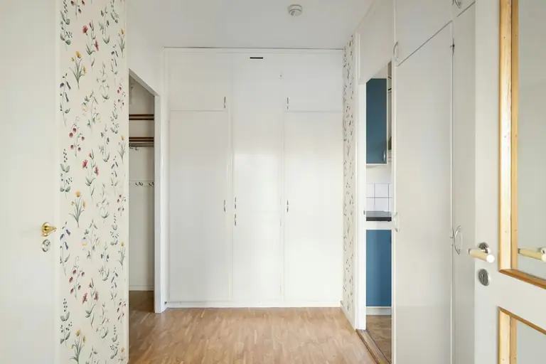 A long hallway with a white door and floral wallpaper