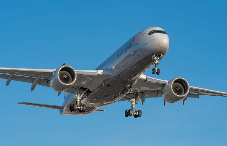 Airplane in flight against a clear blue sky, landing gear out.