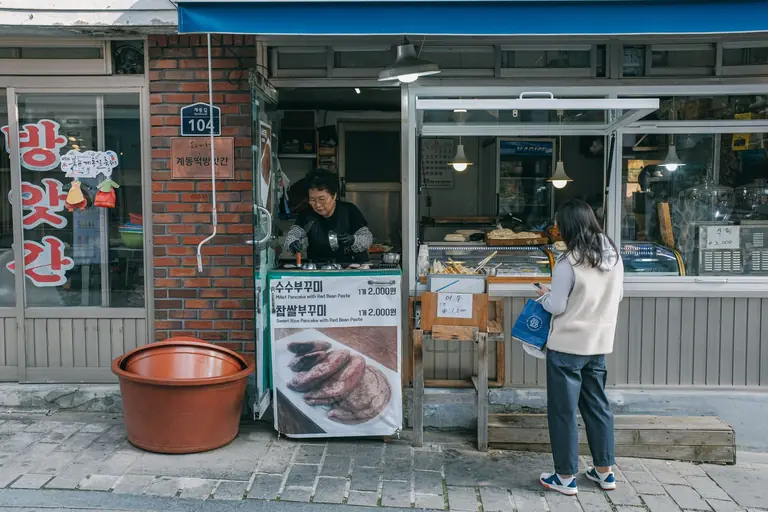 A woman purchasing street food from a vendor in Seoul, capturing urban life.