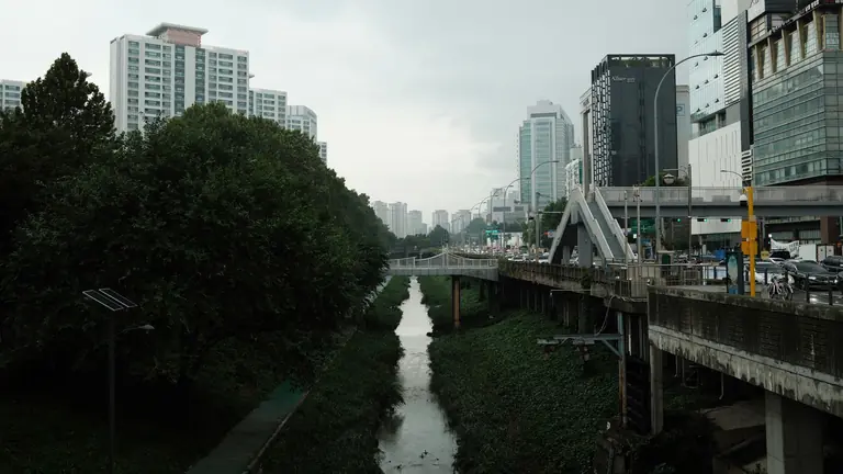 A vibrant cityscape featuring modern skyscrapers, lush greenery, and a bridge over a canal.