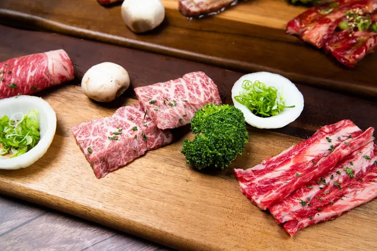 Close-up of assorted Wagyu beef slices with broccoli, mushrooms, and scallions on a wooden tray.