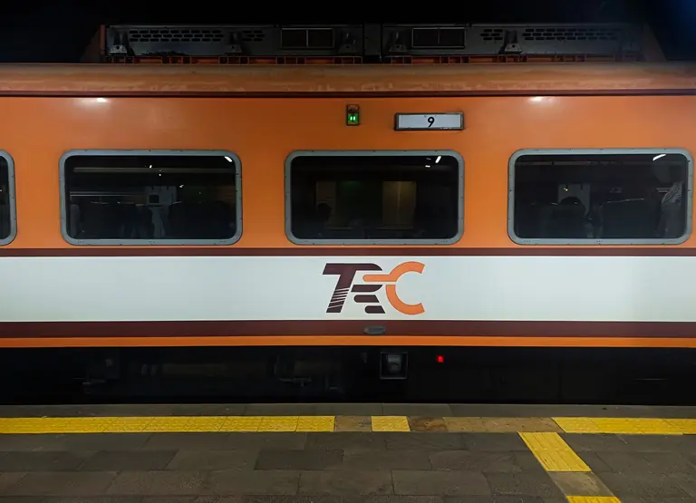 Orange train with TEC logo stopped at a station platform during nighttime.