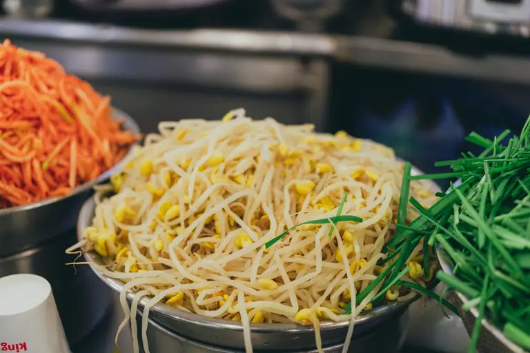 Fresh bean sprouts, carrots, and chives in Seoul street market setting.