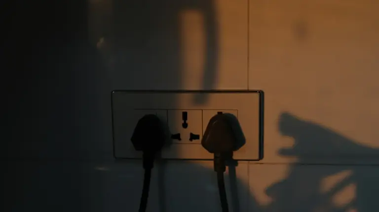 Electrical wall socket with two plugs and dramatic light shadows.